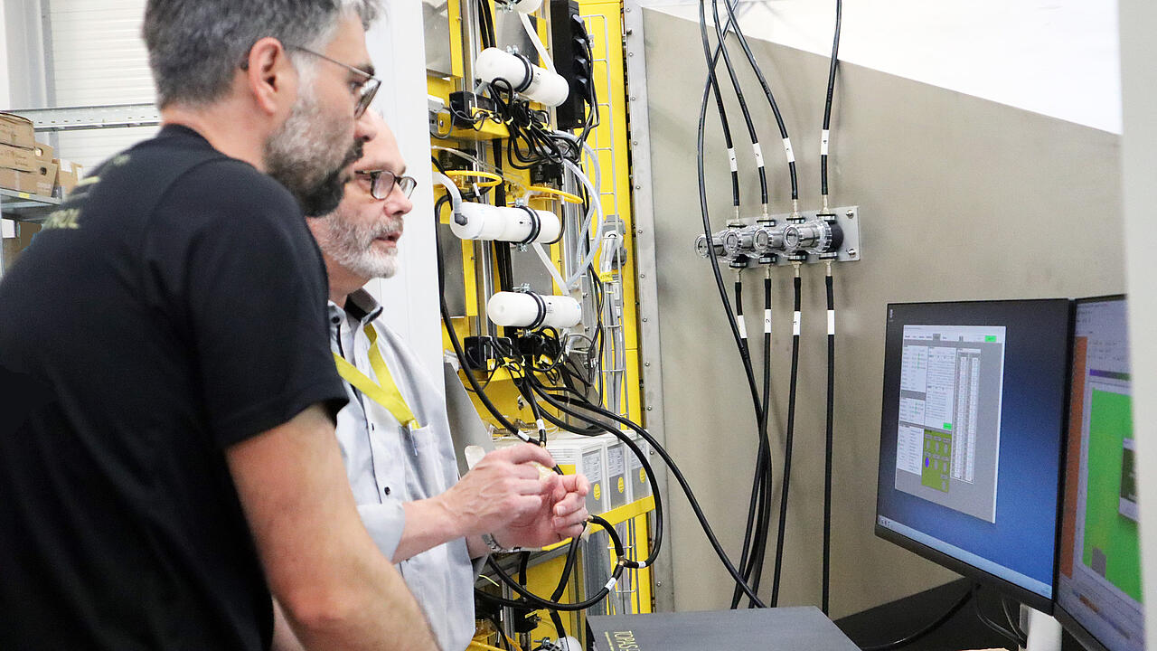 Two men talking in front of screens at a production facility